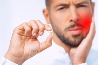 Man holding an extracted tooth while experiencing jaw pain from impacted wisdom teeth before removal at Modern Dentistry of Peoria.